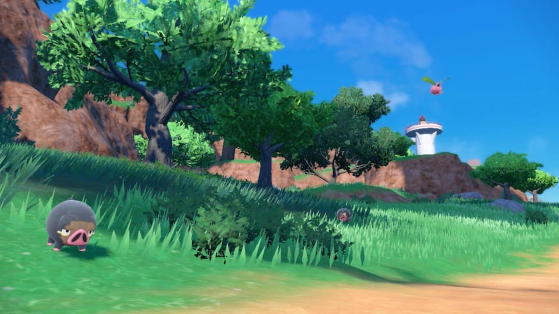 Lechonk, um Pokémon porco ibérico, na grama perto de uma árvore frondosa, com toques de terra em primeiro plano, algumas estruturas de pedra atrás e um céu azul claro, em uma captura de tela de Pokémon Scarlet & Violet.